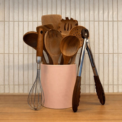 Set of wooden kitchen utensils in a pink container with text 'The Whole Drawer Upgrade' on a tiled wall background.