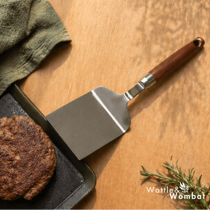 Spatula next to a cooked burger on a wooden surface with 'Wattle & Wombat' branding.