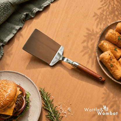 Spatula on a wooden surface with a burger and fries, featuring the Wattle & Wombat logo.