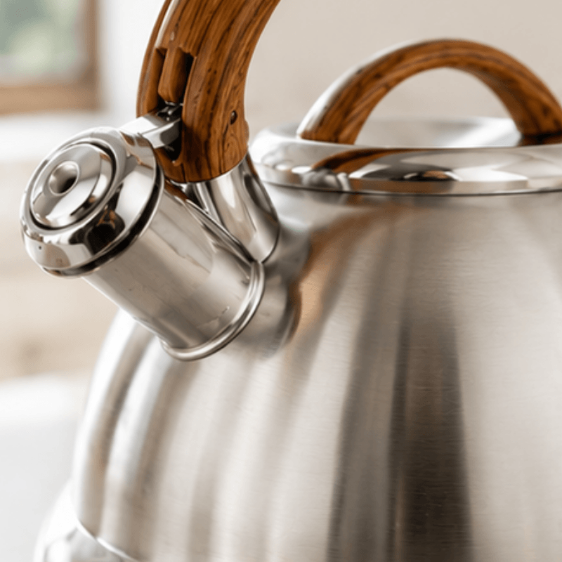 Stainless steel kettle with wooden handles on a blurred background