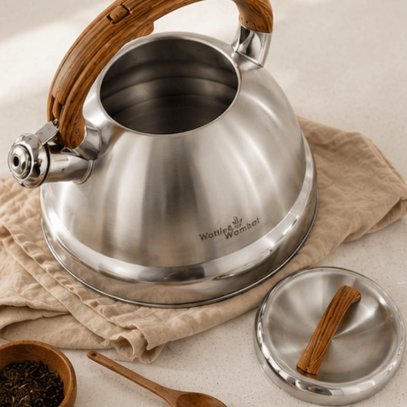 Stainless steel kettle with wooden handle on a beige cloth, surrounded by tea accessories.